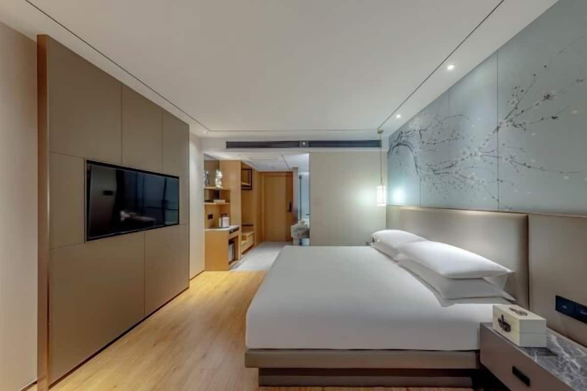 Habitación de hotel moderna con una cama grande, televisión de pantalla plana, estanterías integradas y una pared decorativa de mármol.