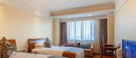 A hotel room with two beds, a television, a desk, and a window with curtains.