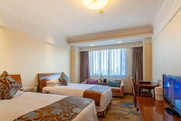 Habitación de hotel con dos camas, televisión, escritorio y ventana con cortinas.