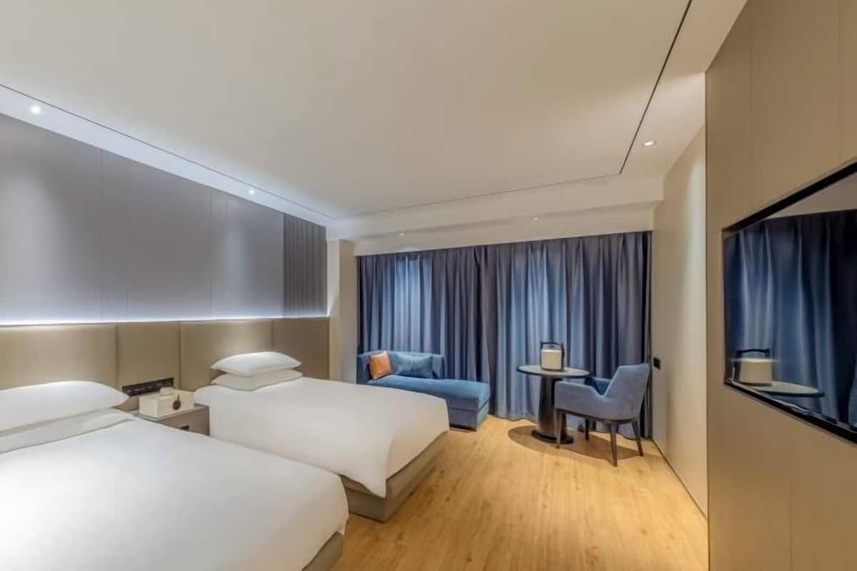 Una habitación de hotel moderna con dos camas, una mesita, una silla y un ventanal con cortinas.