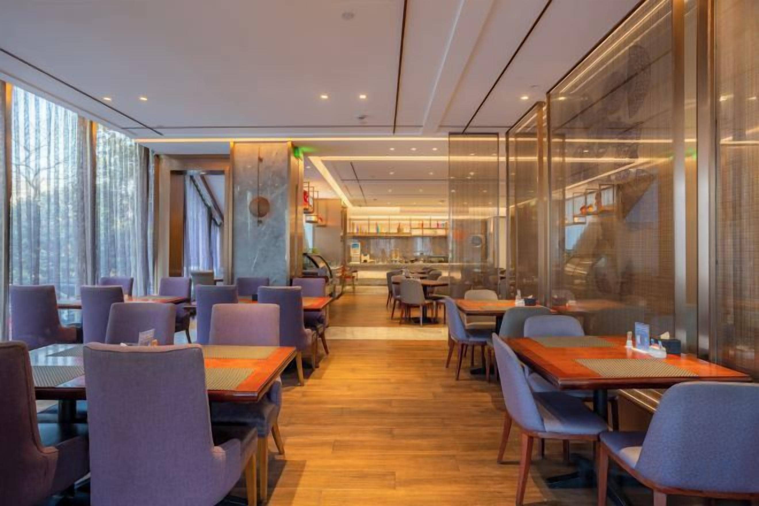 A modern restaurant with a long counter, multiple tables, and chairs. There is a kitchen area in the background.