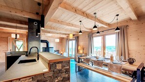 A modern kitchen with a stone island, wooden ceiling beams, and a dining area with a view. - Nice home in Labaroche with sauna (Labaroche)