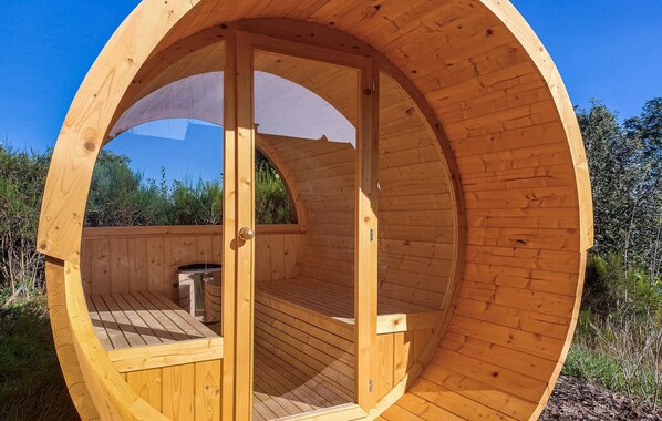 Une structure en forme de dôme géodésique, faite de bois, avec une terrasse en bois et une porte donnant accès à l’intérieur.