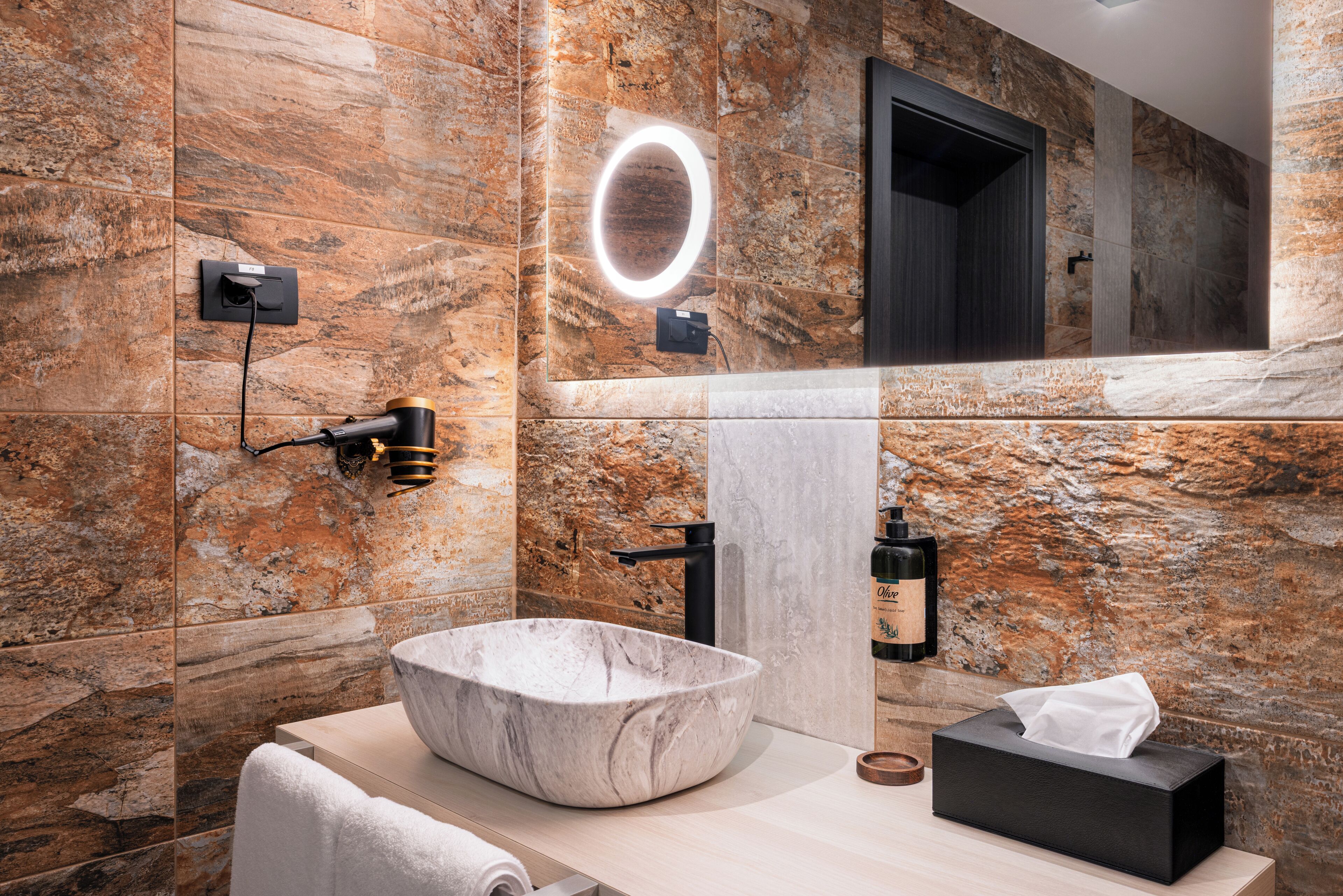 A modern bathroom with a large marble sink, a towel, and a black soap dispenser.