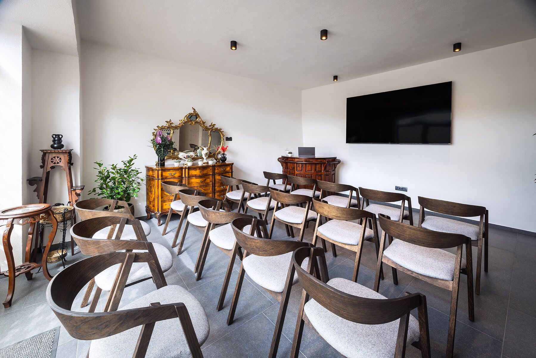 A conference room with wooden chairs, a large mirror, a television, and a wooden cabinet.