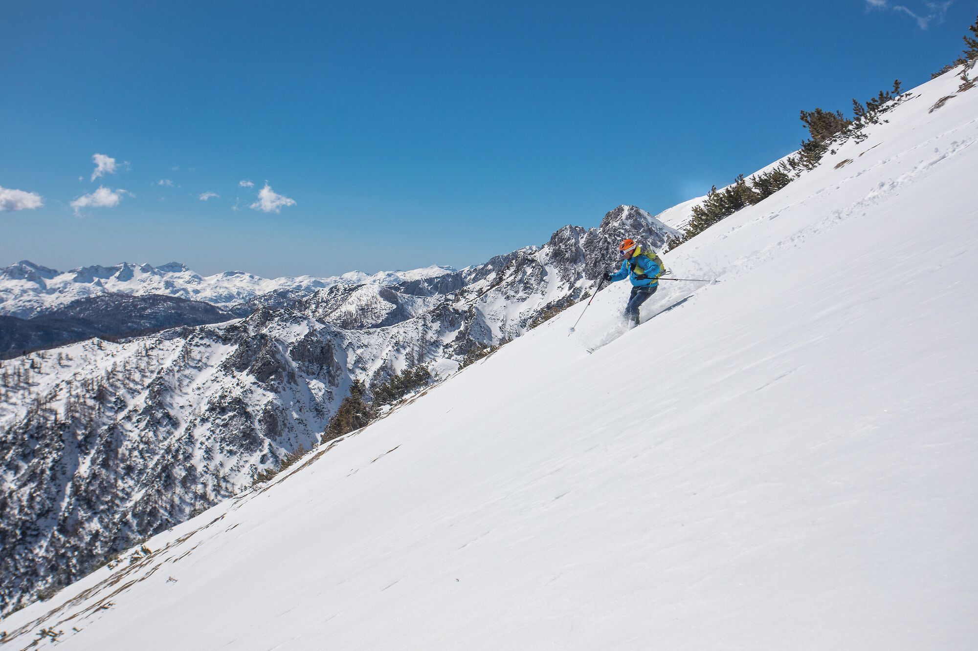 Een persoon skiënd een sneeuwbedekte helling, met bergen op de achtergrond.