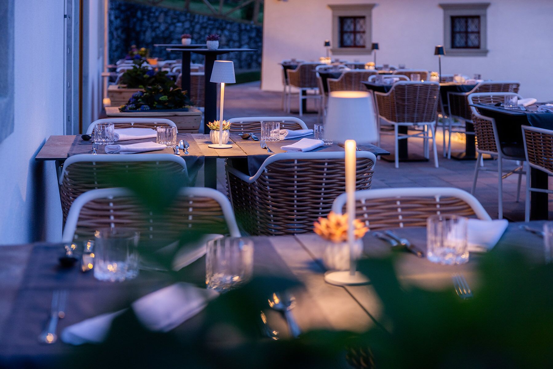 An outdoor dining area with wicker chairs and tables, some with candles.