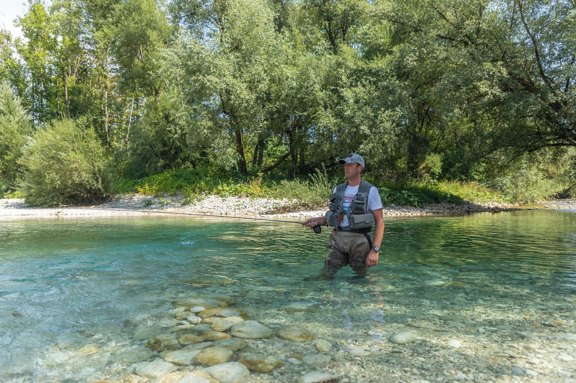A man standing in a clear river surrounded by trees.