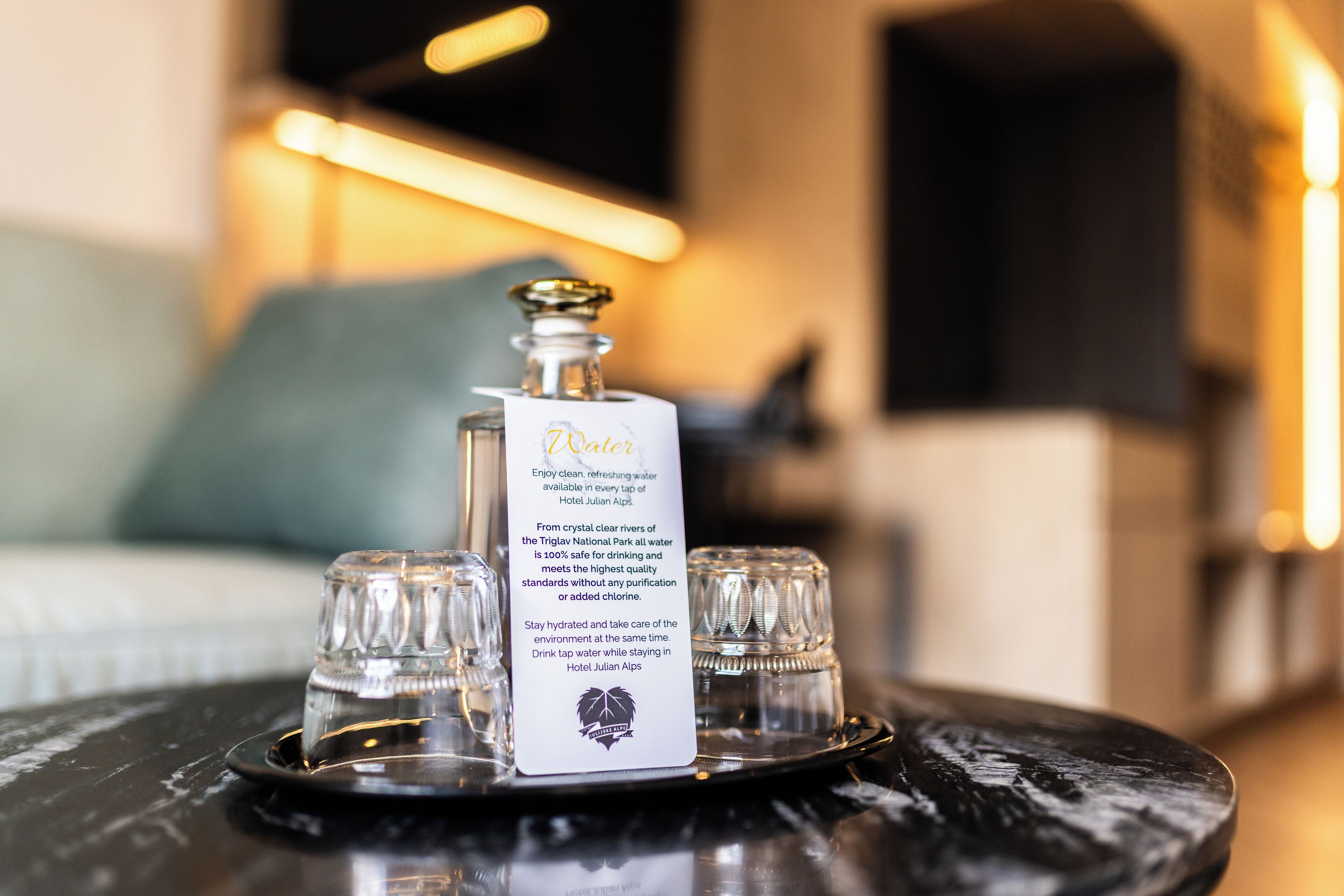 Une bouteille d’eau avec une étiquette, posée sur un plateau avec trois verres.