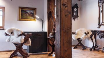 A room with wooden flooring, a large wooden pillar, a desk with a lamp, a chair, a clock, and a framed picture on the wall.