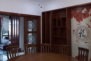 A dining area with a round wooden table, four wooden chairs, a glass partition with a clock, and a decorative wall with Chinese characters. - Moganshan Yashan Inn (Deqing)