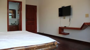 A bedroom with a bed, a wooden door, a television mounted on the wall, and a small wooden shelf. - Moganshan Yashan Inn (Deqing)