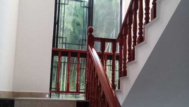 A staircase with wooden balusters and a red handrail, leading to a landing with a large window overlooking greenery. - Moganshan Yashan Inn (Deqing)
