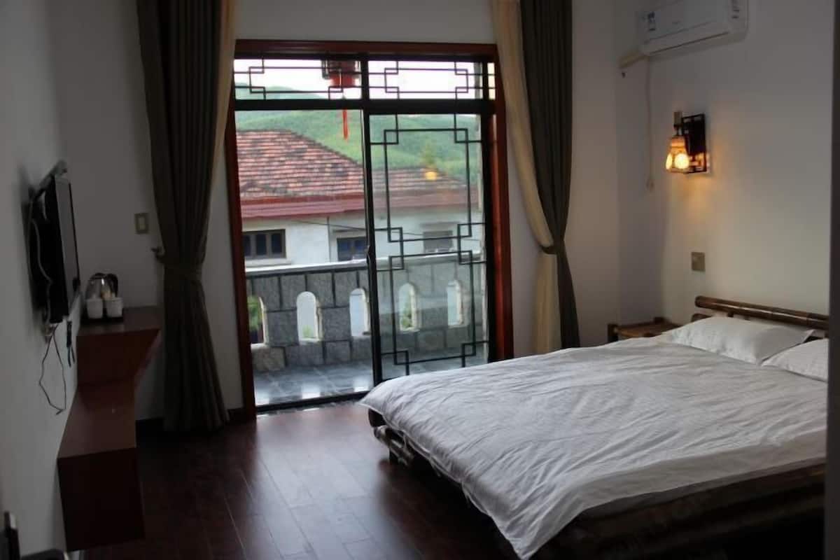 A bedroom with a bed, a TV, a window with curtains, and a view of buildings outside.