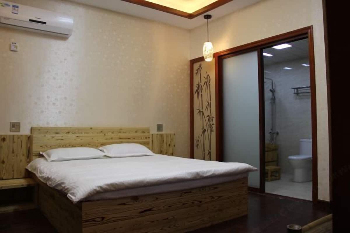 A bedroom with a wooden bed, an air conditioning unit, a sliding glass door to a bathroom, and a hanging light fixture.