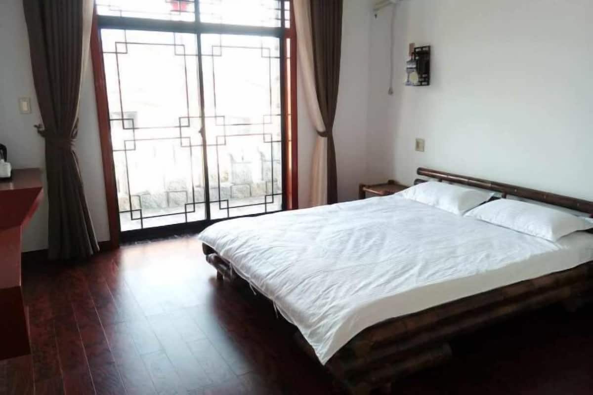 A bedroom with a large bed, a wooden headboard, a nightstand, and a window with curtains.