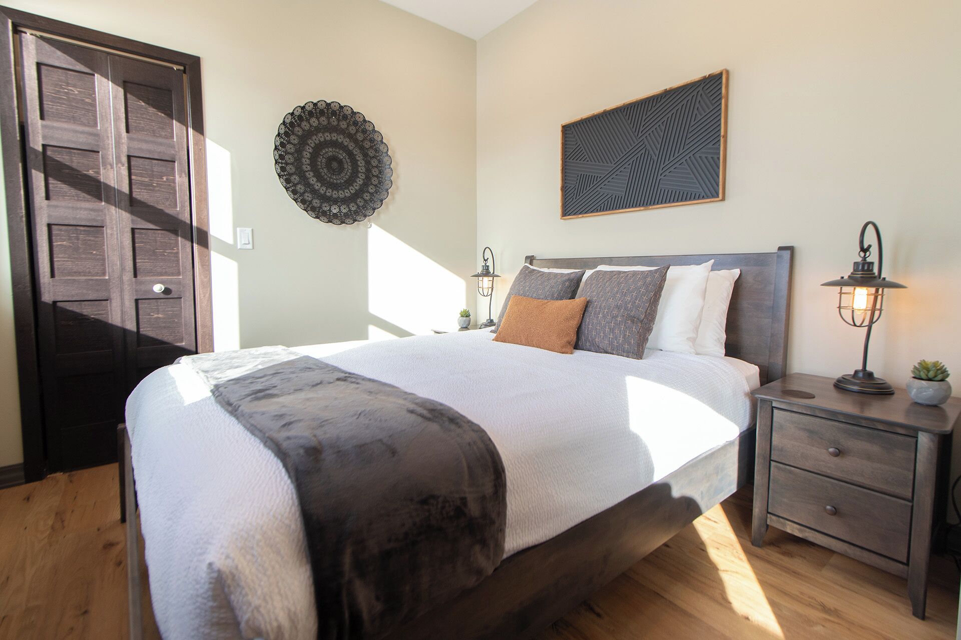A bedroom with a large bed, a nightstand with a lamp, a wall art piece, and a door.