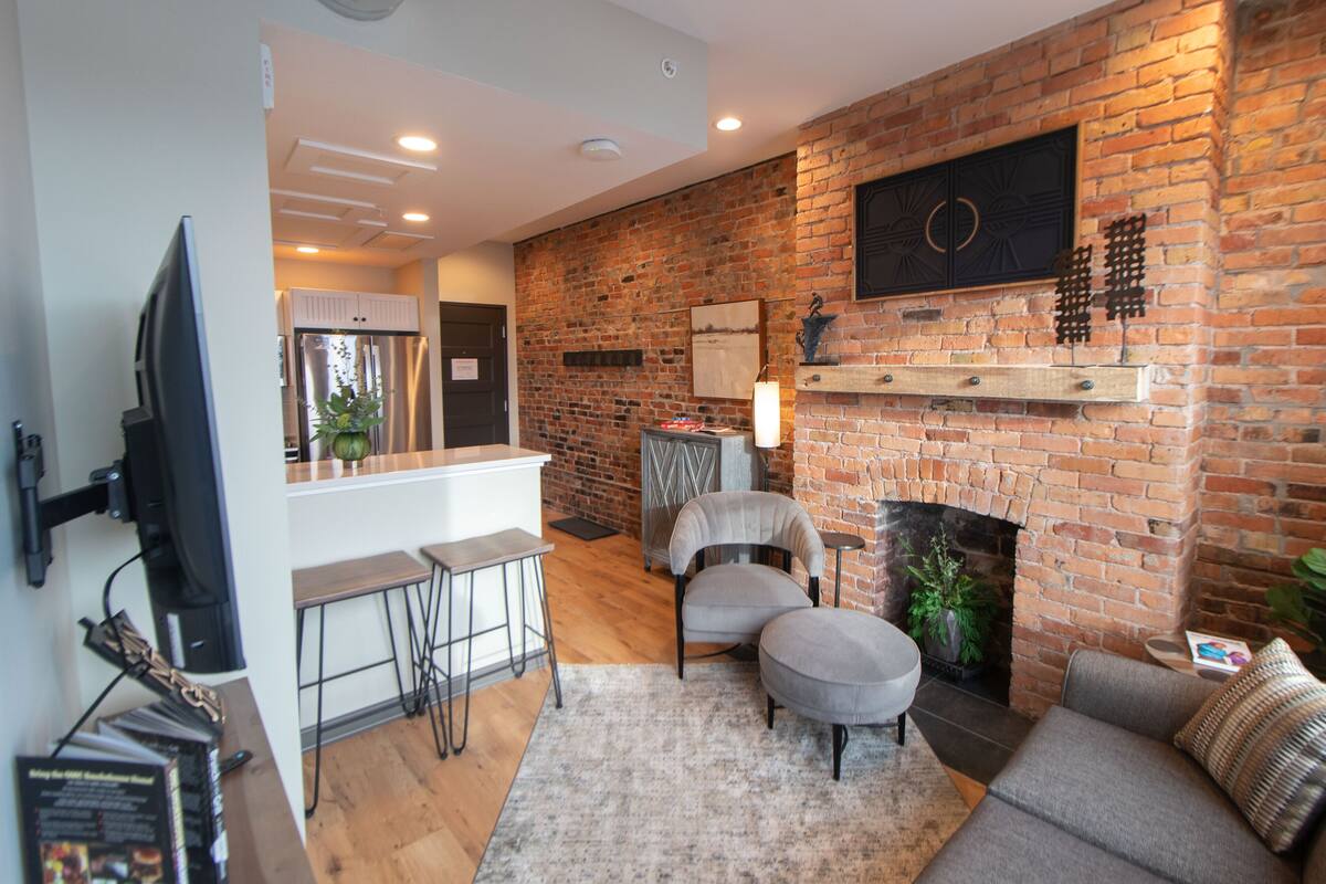 Un salon moderne avec une cheminée en briques, un téléviseur à écran plat fixé au mur et un coin bar avec des tabourets.