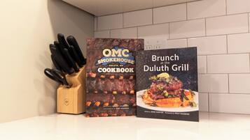 Deux livres de recettes sont posés sur un plan de travail de cuisine, à côté d’un bloc à couteaux : l’un s’intitule « OMC Smokehouse Duluth, MN Cookbook » et l’autre « Brunch at the Duluth Grill ».