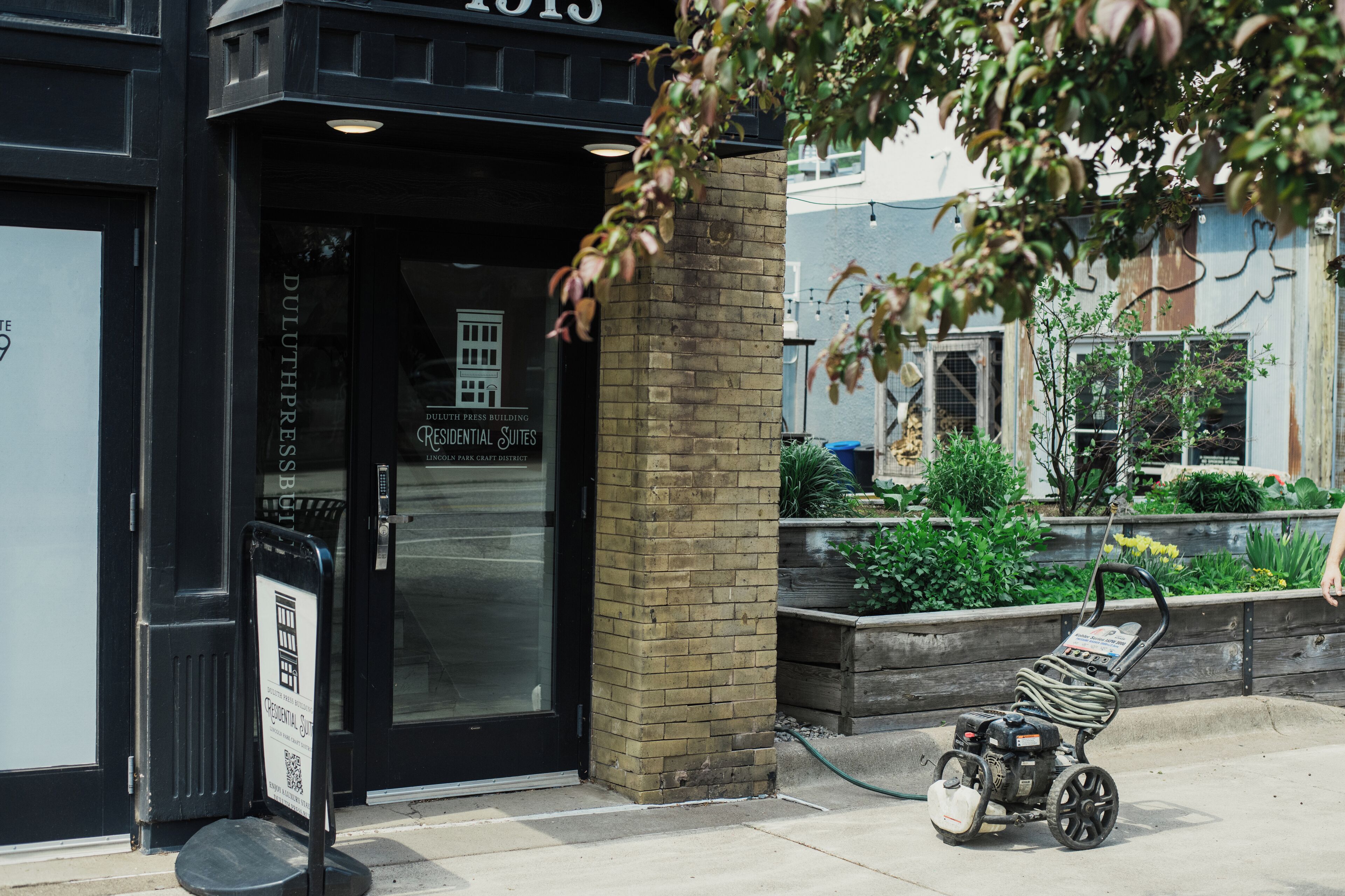 A building entrance with a sign for 'Duluth Press Building Residential Suites' and a power tool on the sidewalk.