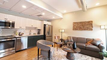 A modern kitchen with stainless steel appliances, a dining area with a round table and chairs, and a living room with a sofa and a coffee table.
