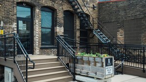 Un bâtiment en briques avec un escalier menant à une porte, une échelle de secours et un jardinier avec une pancarte.