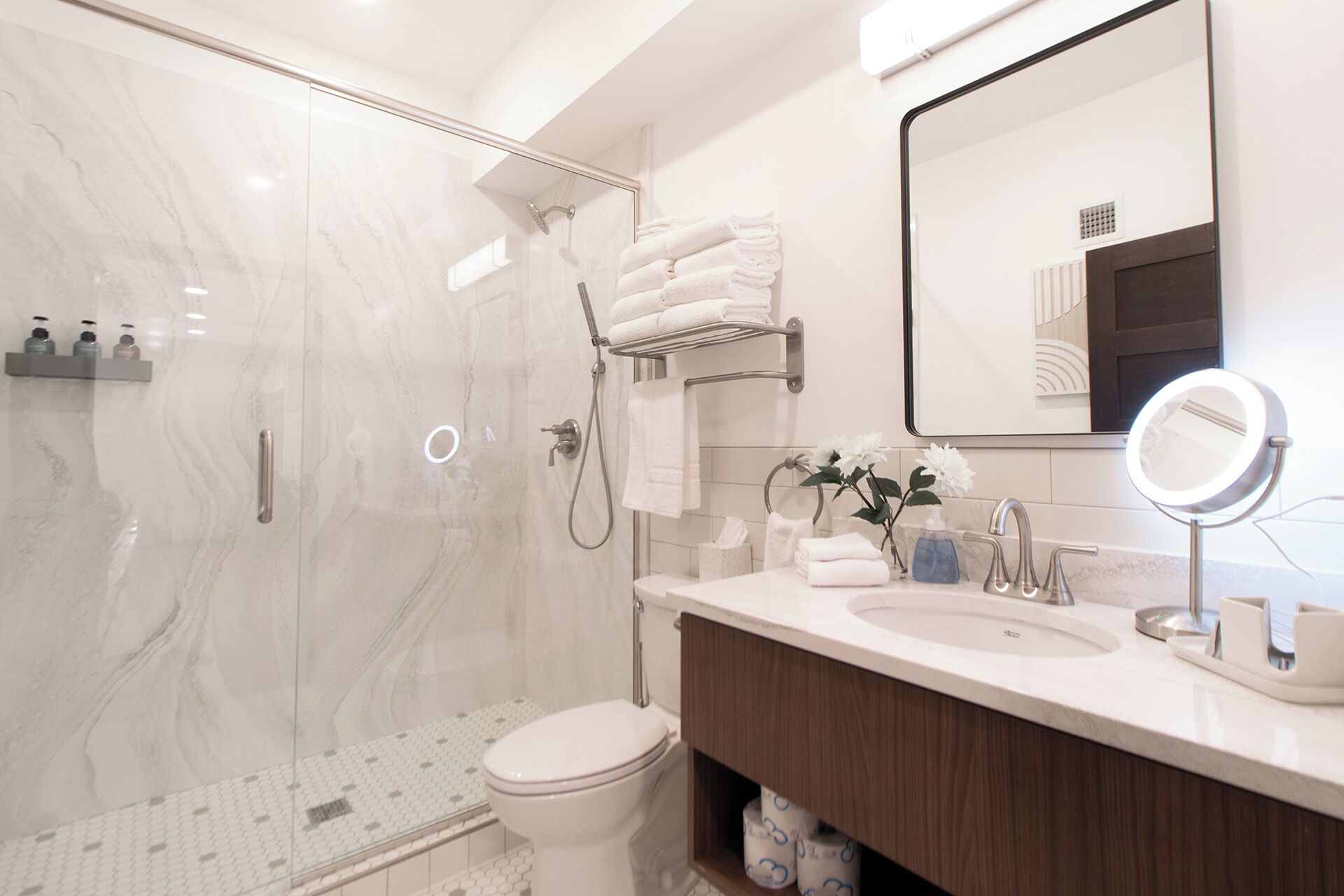 A modern bathroom with a glass-enclosed shower, a toilet, a sink with a vanity, and a mirror.
