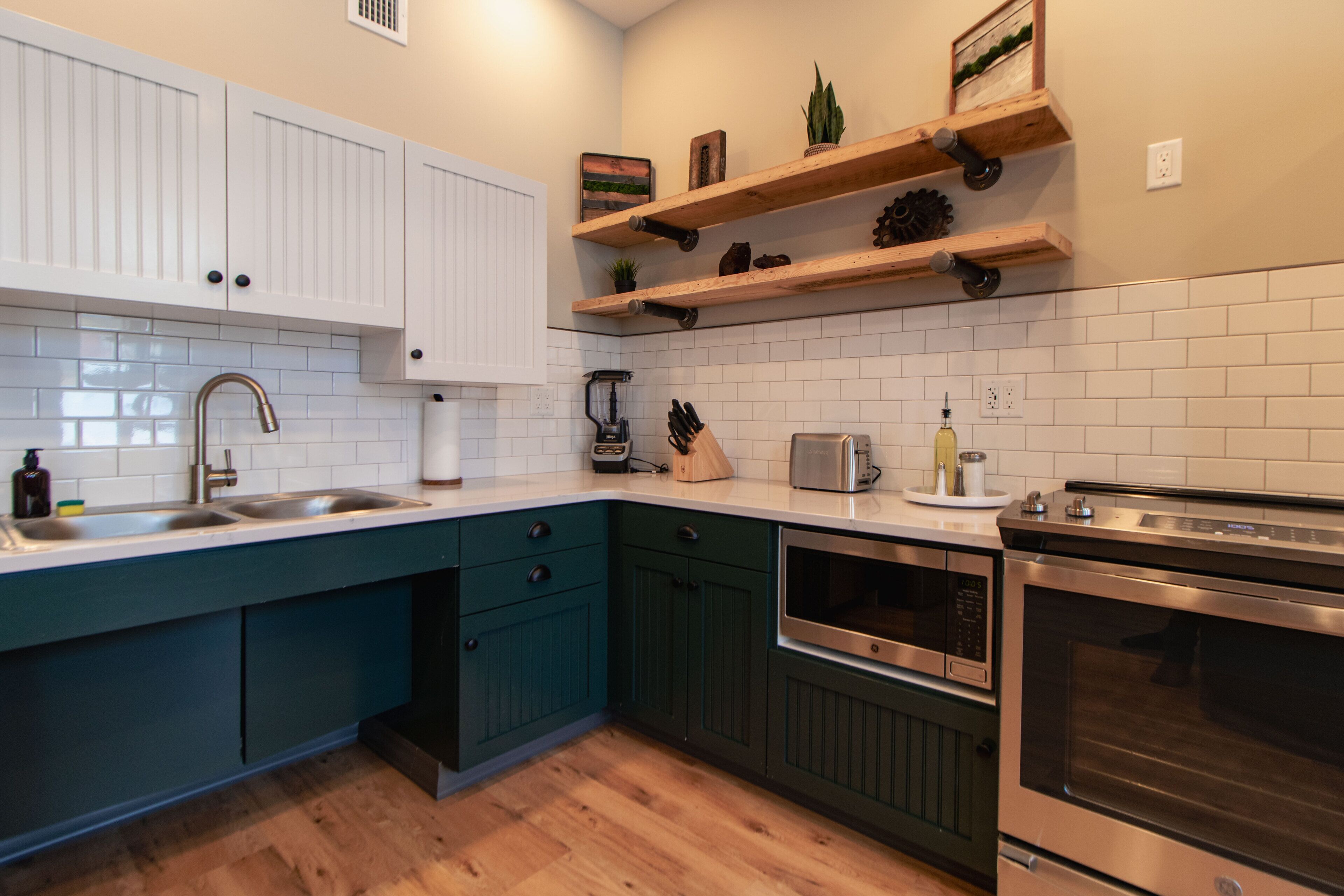 Una cocina moderna con armarios blancos, encimeras verde mar y electrodomésticos de acero inoxidable.