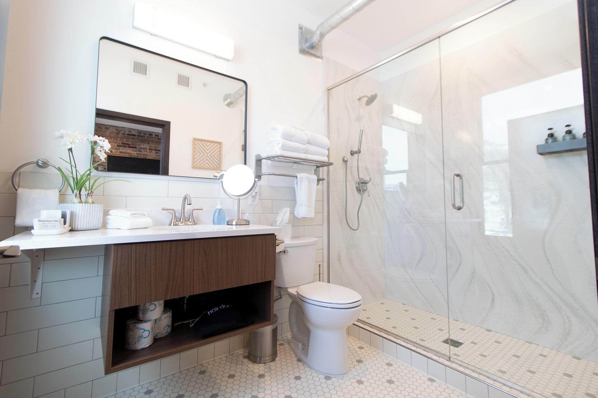 A modern bathroom with a glass shower enclosure, a white toilet, and a vanity with a mirror and towel rack.