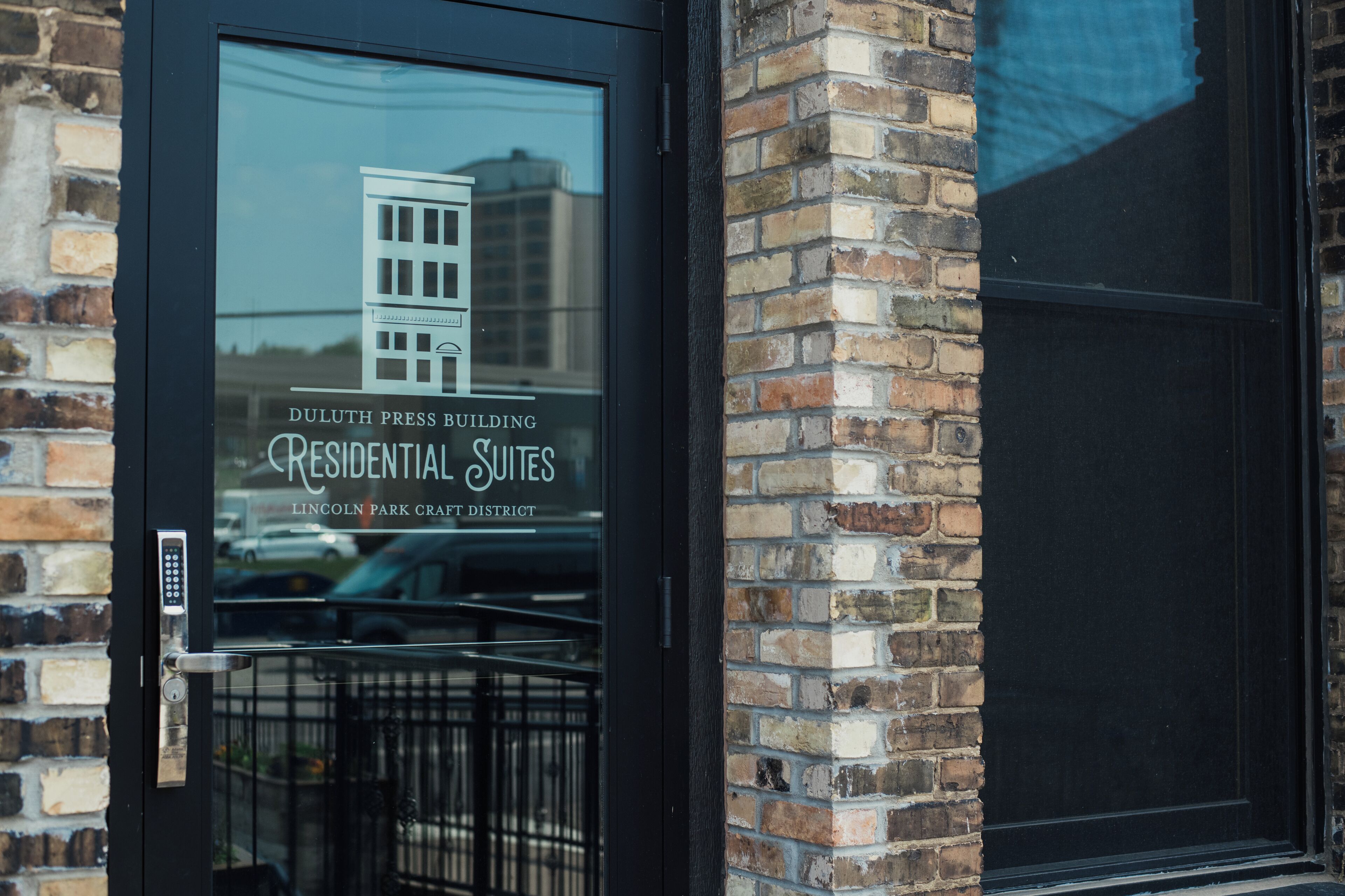 A building with a glass door displaying "Duluth Press Building" and "Residential Suites" in Lincoln Park Craft District.