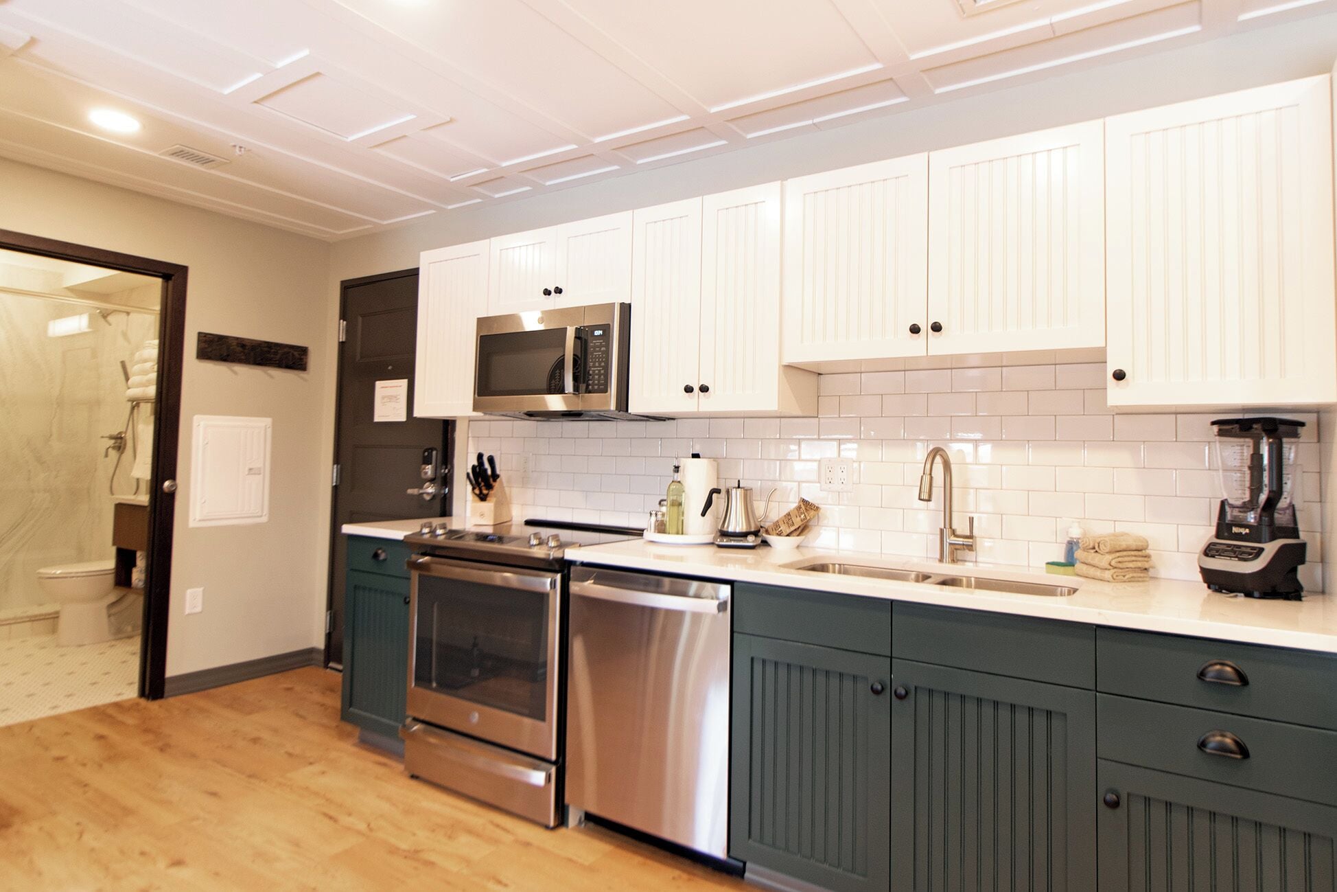 A modern kitchen with white cabinets, stainless steel appliances, and a wooden floor.