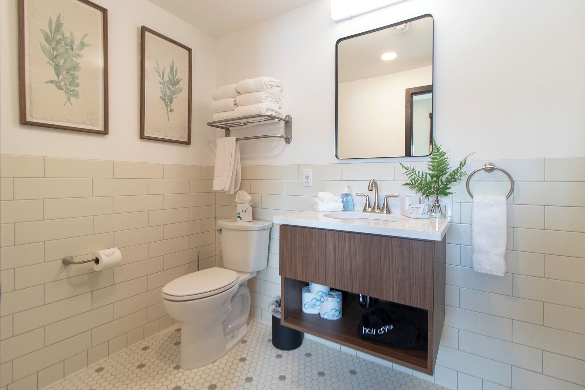 Et badeværelse med toilet, håndvask og spejl. Håndklæder og toiletartikler ligger på håndvaskebordet.
