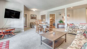 A living room with a round table, wooden chairs, a sofa, and a flat-screen TV mounted on the wall. - Lower-level suite with deck/veranda, garden views, & foosball (Clinton)