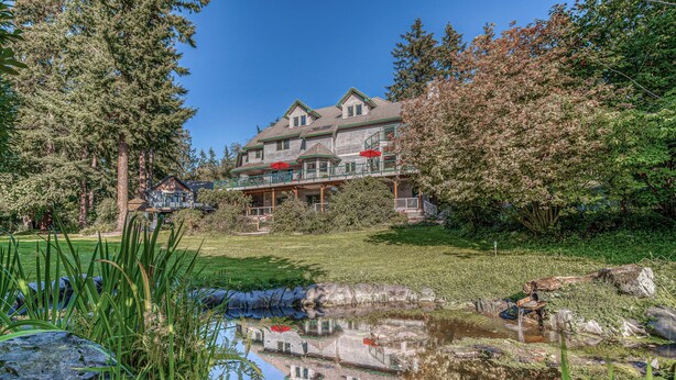 A large house with a pond in front, surrounded by trees and grass. - Lower-level suite with deck/veranda, garden views, & foosball (Clinton)