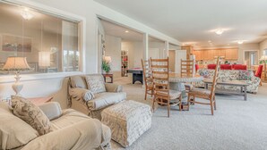 A spacious living room with a sofa, ottoman, and dining area with chairs and a table. - Lower-level suite with deck/veranda, garden views, & foosball (Clinton)