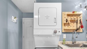Una cocina compacta con lavadora y secadora integradas, un escurreplatos de madera y encimera de granito.