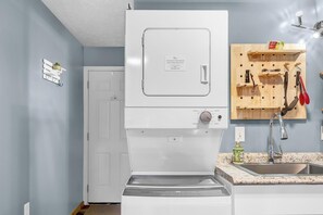 A compact kitchen with a built-in washer and dryer, a wooden utensil rack, and a granite countertop.