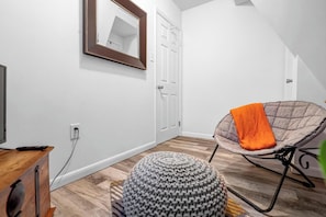 A modern room with a wooden floor, a white door, a mirror, a chair with an orange cushion, and a knitted ottoman. - 2-bedroom cabin with hot tub near George Washington National Forest (Mount Jackson)
