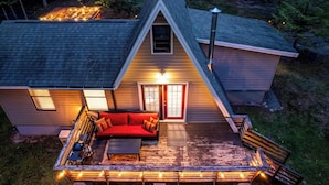 Una casa con techo inclinado, puerta roja y terraza con mobiliario exterior.