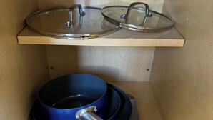 Una cocina con una olla azul sobre una bandeja, un utensilio metálico y un tapa de vidrio en una repisa.