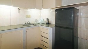 A kitchen with white cabinets, a black refrigerator, and a glass countertop. - RedDoorz @ Broadway Court Apartelle II Quezon City (Quezon City)