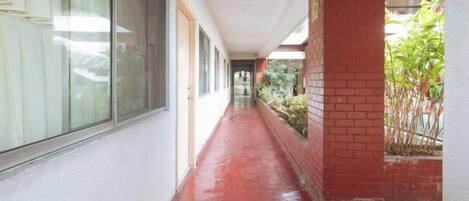 A corridor with a red floor, large windows, and a brick wall on one side.