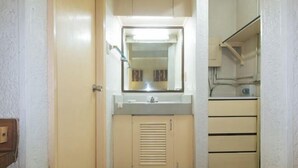 A narrow hallway with a door on the left, a mirror above a sink, and a small cabinet with drawers. - RedDoorz @ Broadway Court Apartelle II Quezon City (Quezon City)