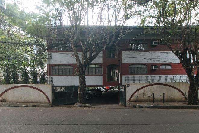 A building with a gated entrance, a tree in front, and a car parked inside.