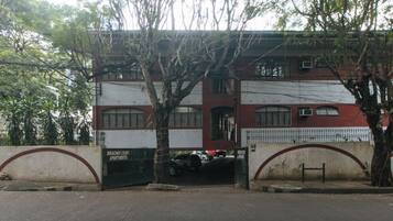A building with a gated entrance, a tree in front, and a car parked inside.