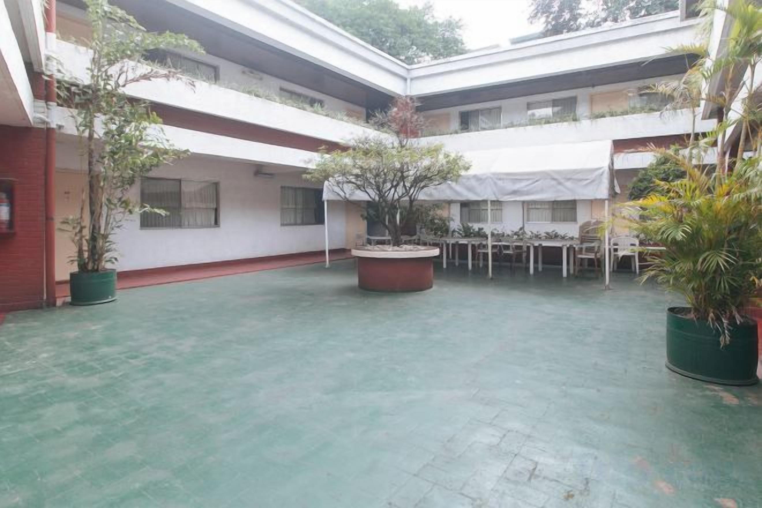 A courtyard with a covered seating area, potted plants, and a building with multiple floors.