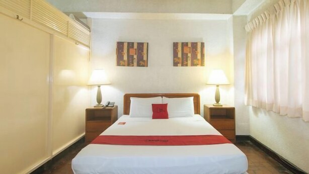 A hotel room with a large bed, two bedside tables, a red accent pillow, and two wall-mounted lamps. - RedDoorz @ Broadway Court Apartelle II Quezon City (Quezon City)