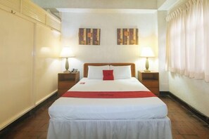 Habitació d'hotel amb un llit gran, dues taules de nit, un coixí vermell decoratiu i dues làmpades penjades a la paret.