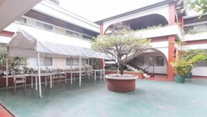 A courtyard with a covered dining area, a central planter with a tree, and a staircase leading to an upper level. - RedDoorz @ Broadway Court Apartelle II Quezon City (Quezon City)