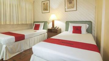 A hotel room with two beds, each with a red bedspread and white bedding. There is a nightstand with a lamp between the beds.